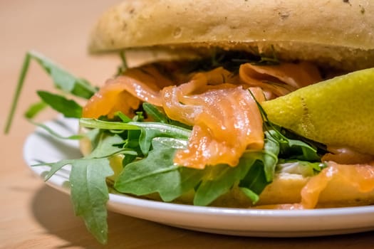 Breakfast bun on a plate, filled with smoked salmon and rocket salad