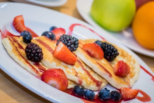 Breakfast meal consisting of pancakes with maple syrup, jam and berries