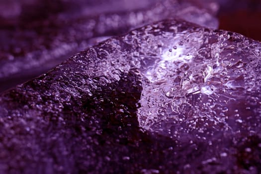 A chunk of ice with frozen air bubbles in the water. A small iceberg in the water in Ultra Violet