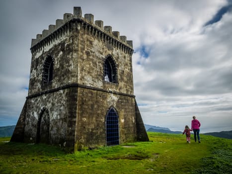 Mother and daughter walking to the small old castle on top of a mountain from where there is a stunning view of the Furnas