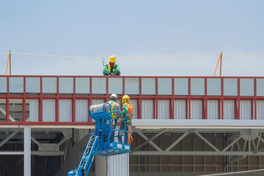 Workers in a baskets are installing sheet, building a factory.