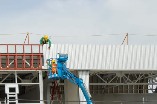 Workers in a baskets are installing sheet, building a factory.