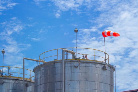 Large steel tank with chemical substance with wind direction indicator. With blue sky