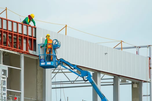 Workers in a baskets are installing sheet, building a factory.