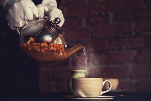 Pouring tea with sea buckthorn honey and herbs in glass teapot