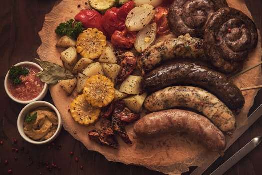 Grilled different meat and fish sausages with vegetables and spices on wooden background