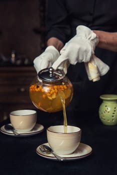 Pouring tea with sea buckthorn honey and herbs in glass teapot