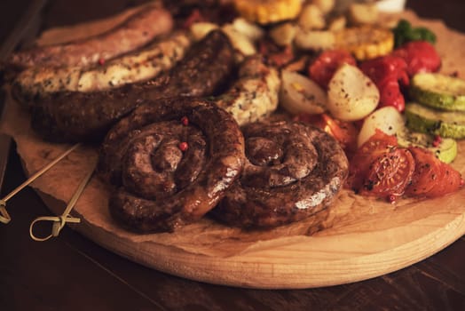 Grilled different meat and fish sausages with vegetables and spices on wooden background