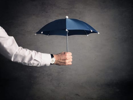 Businessman holding a small blue umbrella, protection or security concept image