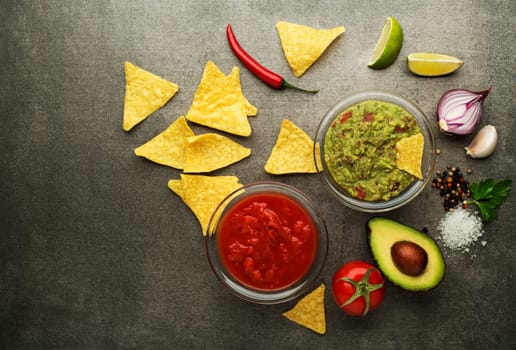 Avocado guacamole and tomato salsa with fresh ingredients on table