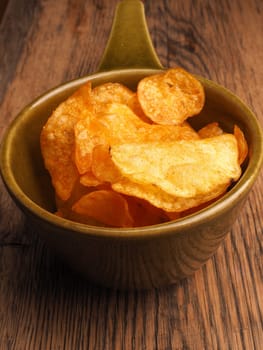 Potato chips in a green ceramic bowl on a wooden table