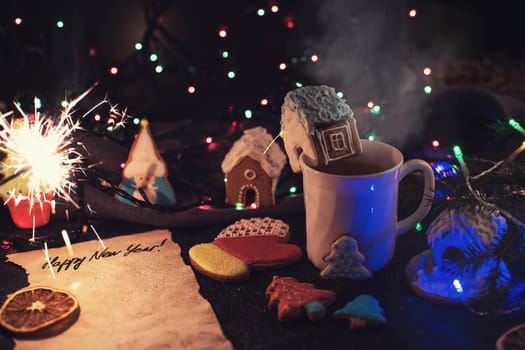 Christmas cookies and cup of tea on dark color bokeh lights background
