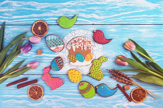 Tulips and gingerbread cookies on white and blue wooden background for Easter.