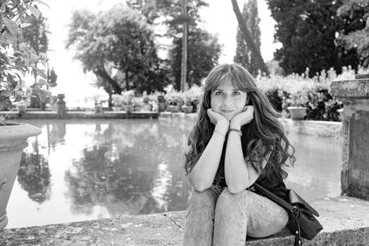 Nice girl with long hair posing near an artificial lake and a lemon tree