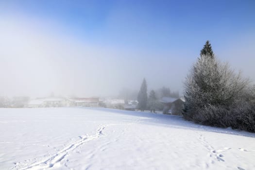 A cold winter day with snow,sun and fog over a city