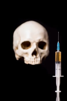 Syringe with brown liquid and blurry skull isolated on black background