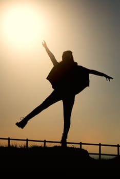 Girl in silhouette over a fence at sunset