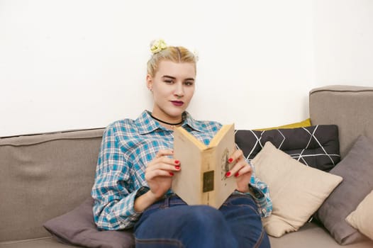 young beautiful girl reading a book sitting on a sofa in the room