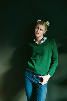 studio portrait of a girl. hipster young beautiful woman in a green sweater and blue jeans, while in the room
