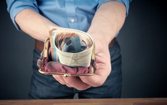 Businessman with an open wallet filled with bank notes, financial concept