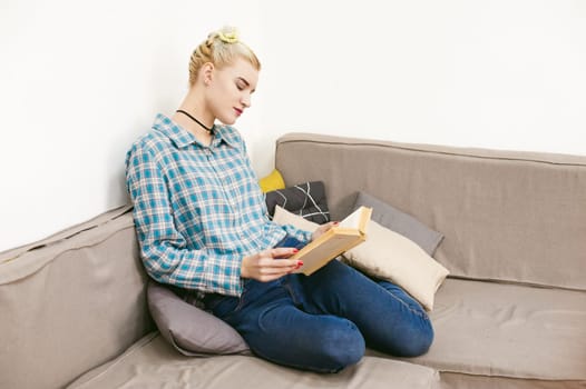 young beautiful girl reading a book sitting on a sofa in the room