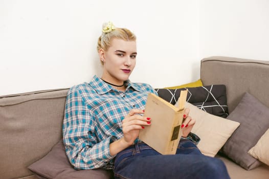 young beautiful girl reading a book sitting on a sofa in the room