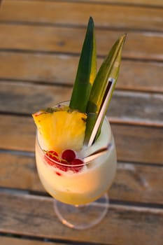 Fruit cocktail with alcohol, pineapple and red currant on wooden table.