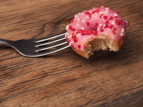 Pink sweet donut with a fork on a wooden table, unhealthy food concept with space for text