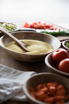 Couscous in wooden bowl on table with other ingredients.