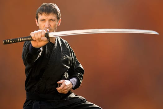 Sitting ninja in black kimono is holding his sword on brown background.