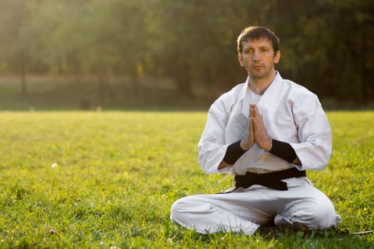The sitting martial arts master is greeting outdoors in nature.