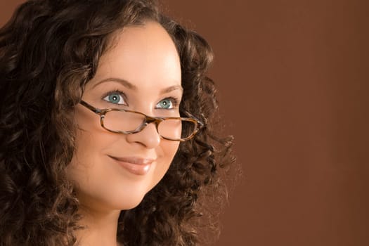 Portrait of woman with glasses and curly hair on brown background.