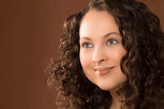 Beauty portrait of smiling woman with curly hair and perfect natural make-up, brunette, hairstyle on brown background.