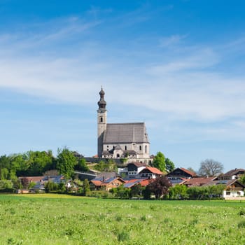 Spring scenery with rural Catholic church and small Bavarian village. Square stock photo.