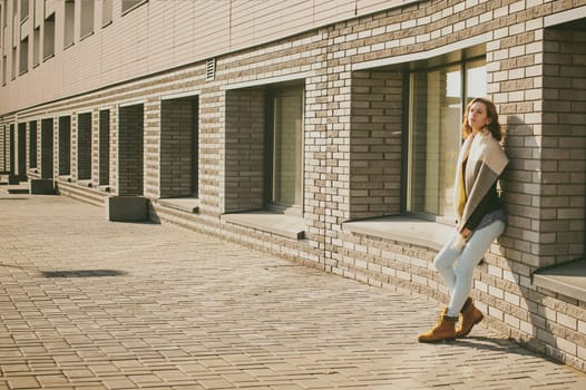 Portrait of young woman walking outdoors on warm autumn afternoon. Against a brick wall background