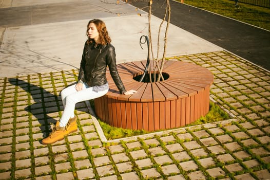 Portrait of young woman walking outdoors on warm autumn afternoon. Sitting resting