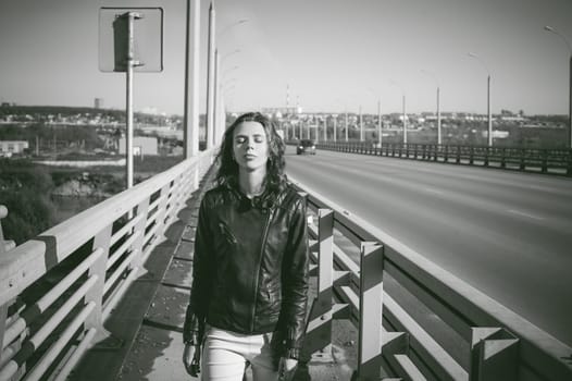girl goes on road bridge. lonely young woman in black Leather jacket autumn, walking over the bridge which goes transport.