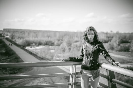 portrait of a beautiful young woman with long thin hair, a leather jacket, blue jeans. warm autumn sunny day on the stairs of the bridge.