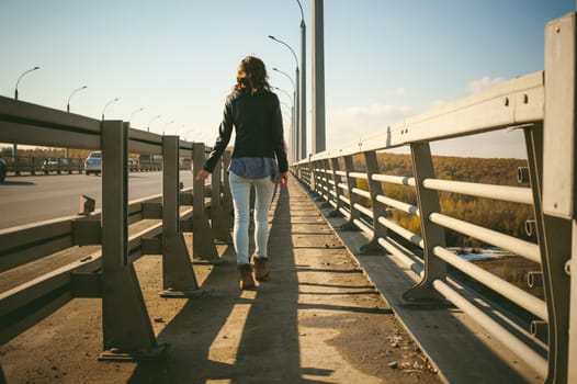 girl goes on road bridge. lonely young woman in black Leather jacket autumn, walking over the bridge which goes transport.