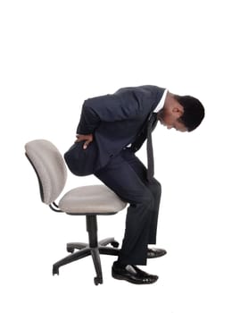 A young business man in a suit getting up from his office chair holding .his back for back pain, isolated for white background.
