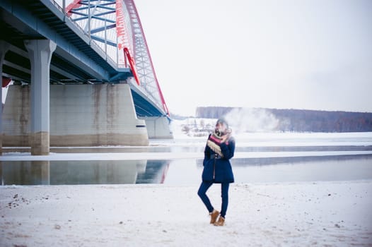 vaping girl. winter street portrait of a woman hipster, purple-dyed hair, a gray knitted hat and scarf. woman smokes an electronic cigarette in the street near the snow-covered river