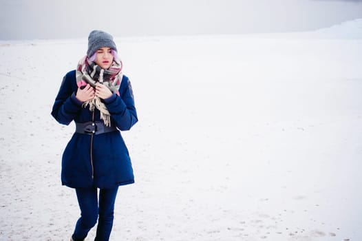 vaping girl. winter street portrait of a woman hipster, purple-dyed hair, a gray knitted hat and scarf. woman smokes an electronic cigarette in the street near the snow-covered river