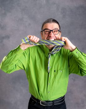 stressed man in green shirt and glasses biting in his necktie and looking crazy in to the camera