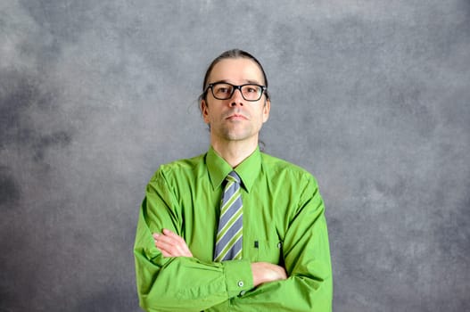young business man in green shirt and necktie with crossed arms in front of gray background