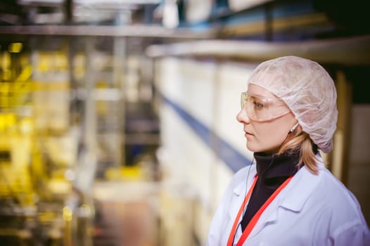 Female worker on the production line of beer factory. portrait of a woman in a white robe, standing on the background of the production line in a factory