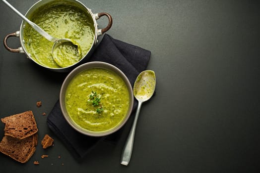 Fresh healthy green soup on black background overhead shoot.