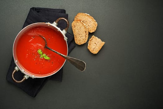 Fresh tomato soup with bread on black background. Top view
