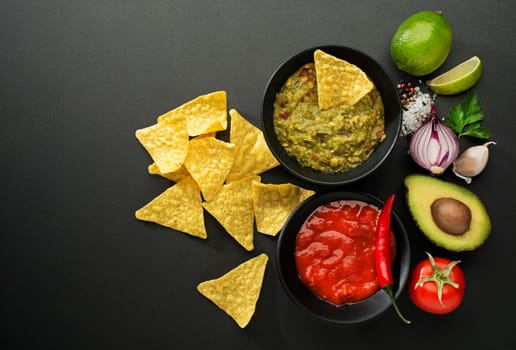 Avocado guacamole and tomato salsa with fresh ingredients on table