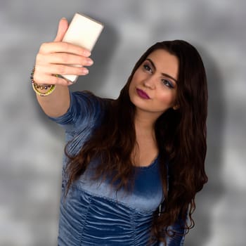 Young attractive woman makes selfie on gray background.