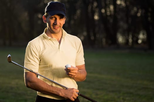 Handsome smiling golfer is holding a golf ball and the putter.